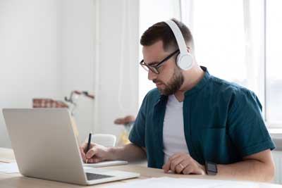 Man with earphones writing notes at desk